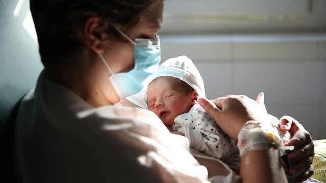 Woman wearing a face mask while holding her newborn baby.
