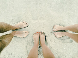 Three pairs of feet on a sandy beach. Travel background.