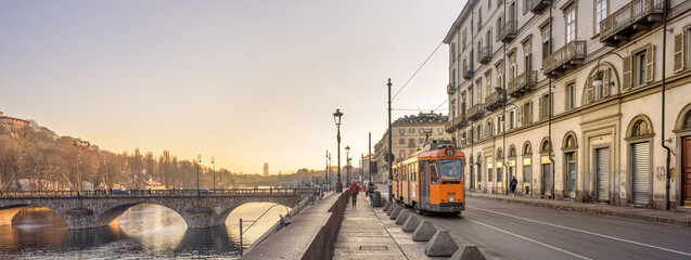 Turin, Italy. February, 15, 2022. View at sunset on the Po river In the distance the ancient Vittorio Emanuele I bridge and a tram passing in Lungo Po Luigi Cadorna street. Banner header. - obrazy, fototapety, plakaty