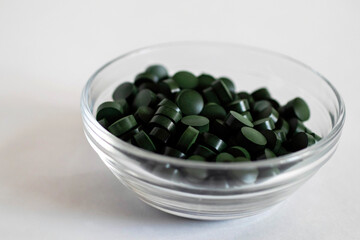 A close-up pile of round green pills in a transparent pill box, shifted to the right.