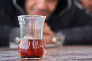 Traditional turkish tea inside traditional slim waisted glass cup, blurred smiley man photo behind the tea glass.