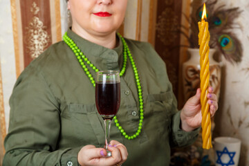 A Jewish woman in a Kisui Rosh headdress with a glass of wine and avdala candles in her hands.