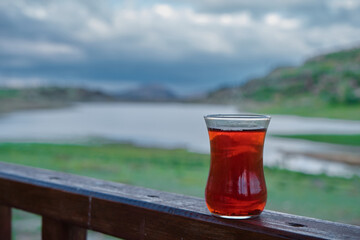 Traditional turkish tea inside traditional glass behind the lake and landscape view from wide angle view.