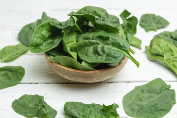 organic spinach leaves in bowl and on white planks