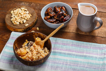 A plate of couscous on a wooden table with a wooden spoon next to dates nuts and a jug of fruit broth. Save a place.