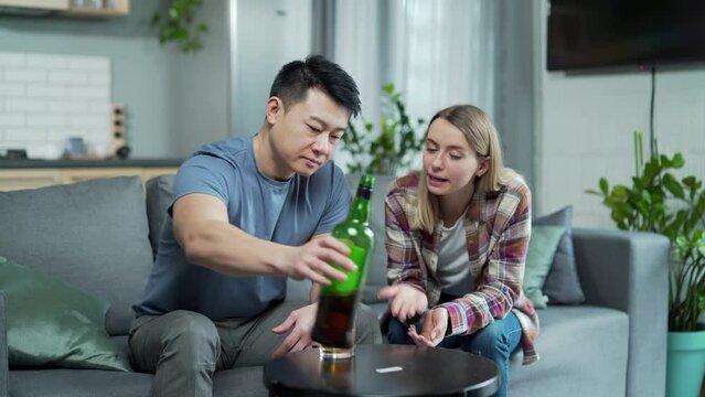 Asian husband is an alcoholic, drinks strong alcohol at home, his wife quarrels with him and tries to interfere, multiracial family at home conflic. problem of alcoholism and addiction to bad habits