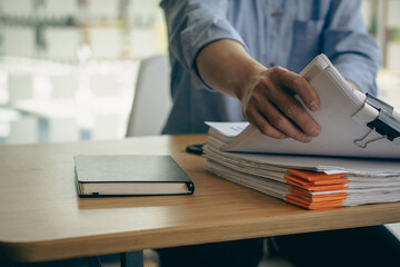 An employee sits at a table full of paper. stamp on the pile of unfinished documents A young...