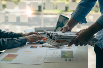 An employee sits at a table full of paper. stamp on the pile of unfinished documents A young account manager's secretary works in the office among piles of paperwork on the table. © ArLawKa