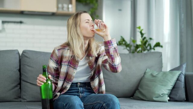 female alcoholism. Lonely woman at home sitting on the couch with a glass of whiskey in his hands and drinking alcohol. Sad grief young alcoholic woman in home. dependence problem concept