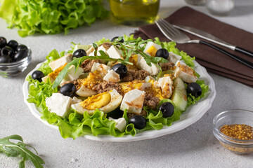 Salad with tuna, cucumber, boiled eggs, olives and feta, served on green salad leaves with Dijon mustard