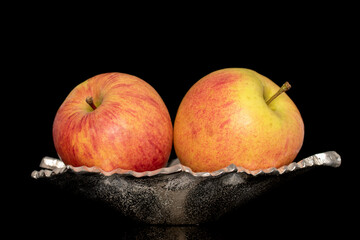 Two juicy organic apples in a metal bowl, close-up, isolated on a black background.