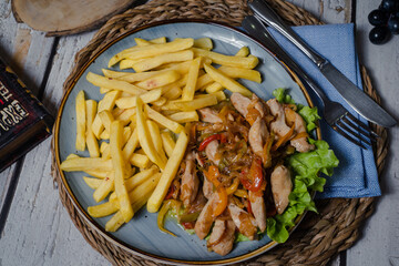 Chicken goulash with vegetables and french fries on a blue dish. Top view - obrazy, fototapety, plakaty