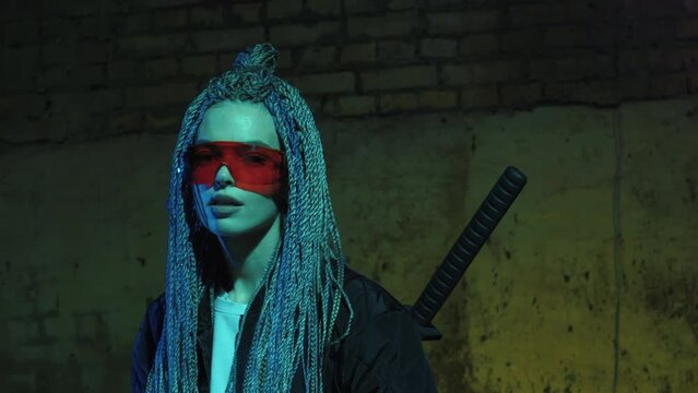 girl with dreadlocks and katanas in red glasses posing against a neon brick wall