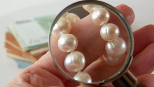 jeweler looking at pearls necklace through magnifying glass on black background, jewerly inspect and verify, pawnshop concept, jewerly shop