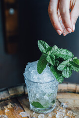 Woman’s hand placing ice in glass mint julep cup