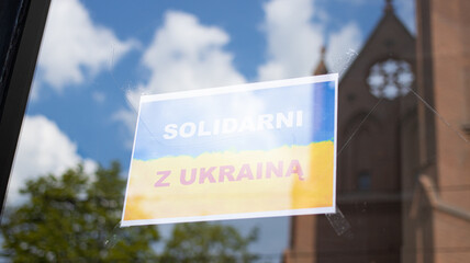 Yellow blue flag poster with inscription solidarni z ukraina translated from polish in solidarity with Ukraine, pasted on a glass shop window. The concept of patriotism and support from Poland