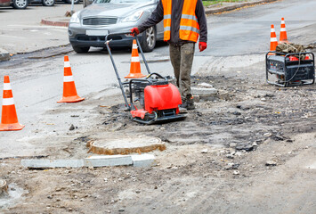A road service worker repairs a section of the carriageway near a sewer manhole. - obrazy, fototapety, plakaty