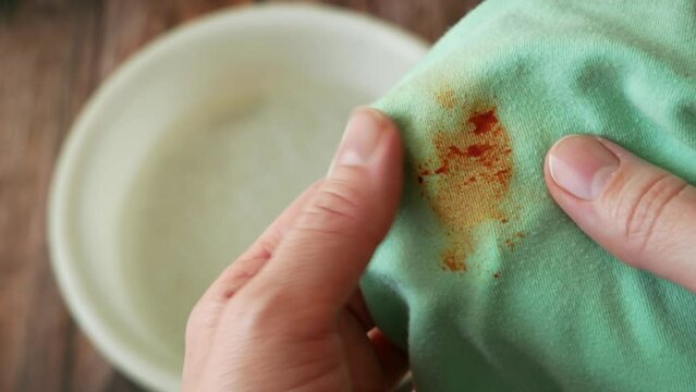 Cleaning laundry manually. Women's hands in gloves washing dirty stained on colored cloth with a stain remover and soak in soapy water