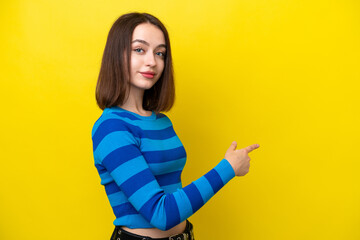 Young Ukrainian woman isolated on yellow background pointing back © luismolinero