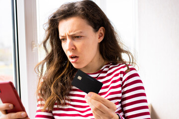 Stressed young brunette woman online buyer holding bank credit card, looking confused on mobile...