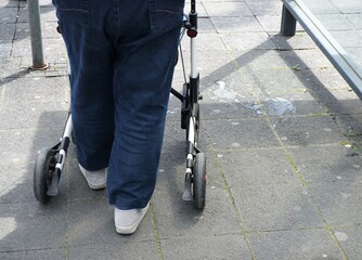 Beine von alter Frau mit Jeans von hinten an Rollator in Stadt 