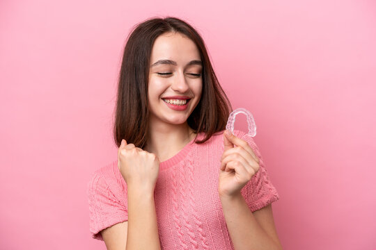 Young Ukrainian woman holding invisible braces isolated on pink background celebrating a victory