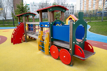 A children's wooden train with a red blue yellow trailer on a yellow playground in the city. Playgrounds, toys, sports.