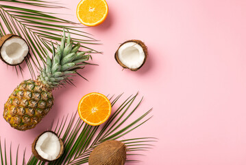 Summer concept. Top view photo of fresh tropical fruits cracked coconuts pineapple cut oranges and palm leaves on isolated pastel pink background with copyspace