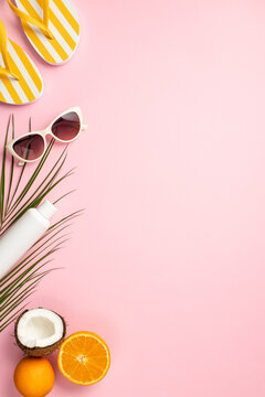 Summer rest concept. Top view vertical photo of sunglasses sunscreen bottle yellow flip-flops coconut oranges and palm leaves on isolated pastel pink background with copyspace
