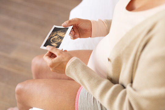 Mid section of caucasian pregnant woman holding ultrasound image of her baby at home
