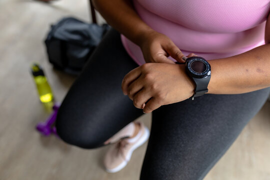 Low section of african american mid adult woman wearing wristwatch while sitting at home