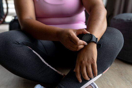 Midsection of african american mid adult woman showing wristwatch while sitting on floor at home