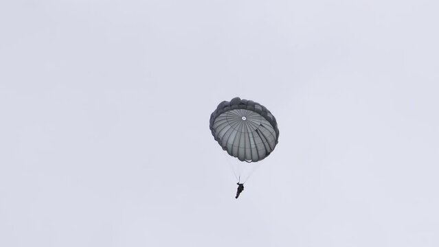 Paratrooper falling to the ground with parachute open  as they float through the air.