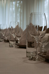 proper serving in restaurant. table covered with white tablecloth, cutlery and glasses on the table. soft beige chairs. Wedding dinner table reception. serving cutlery according to rules of etiquette.