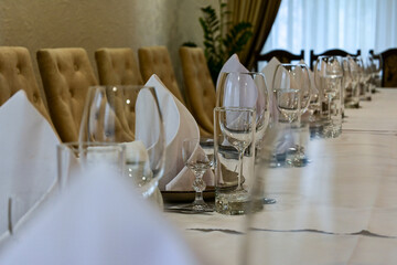 proper serving in restaurant. table covered with white tablecloth, cutlery and glasses on the table. soft beige chairs. Wedding dinner table reception. serving cutlery according to rules of etiquette.