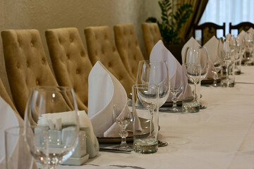 proper serving in restaurant. table covered with a white tablecloth, cutlery and glasses on the table. soft beige chairs. premium restaurant. serving cutlery according to the rules of etiquette.