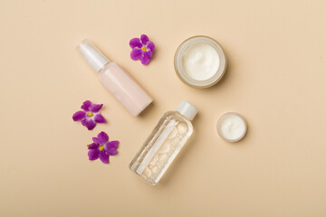 Cosmetic bottles and jars with flowers on color background, top view