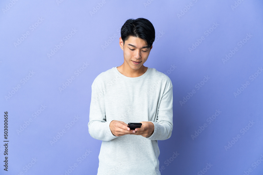 Poster Young Chinese man isolated on purple background sending a message with the mobile