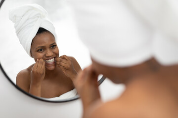 African american mid adult woman looking at mirror using dental floss in bathroom