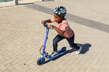 High angle view of african american boy riding push scooter on promenade during sunny day - Powered by Adobe