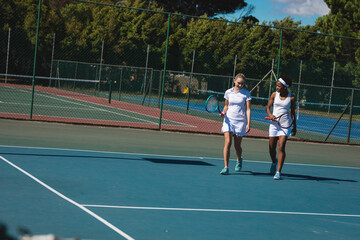 Fototapeta premium Smiling multiracial female players talking while walking at tennis court on sunny day
