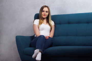 Fototapeta premium Attractive young adult housewife woman sitting on the couch and looking at the camera in her house
