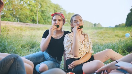 Friends have fun eating watermelon outside the city at a picnic.