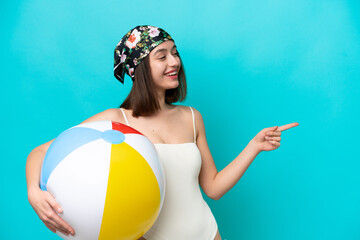 Young Ukrainian woman holding beach ball isolated on blue background pointing finger to the side...