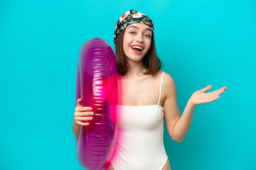 Young Ukrainian woman holding air mattress isolated on blue background with shocked facial expression
