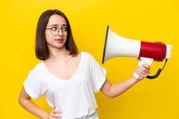 Young Ukrainian woman isolated on yellow background holding a megaphone with stressed expression