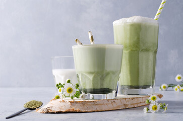 Matcha coffee with milk in glass glasses on a wooden tray on a gray-blue background