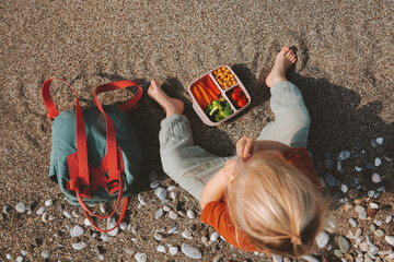 Child with lunch box and backpack outdoor kid eating vegan food on beach picnic outdoor healthy...