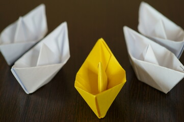Several white paper boats and a yellow one on the table.