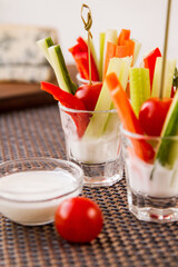 Two glasses of assorted raw vegetables - carrot, celery, cucumber, pepper, cherry tomato with yogurt dip.